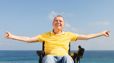 Man sitting in a wheel chair with the sea and clear blue skys behind